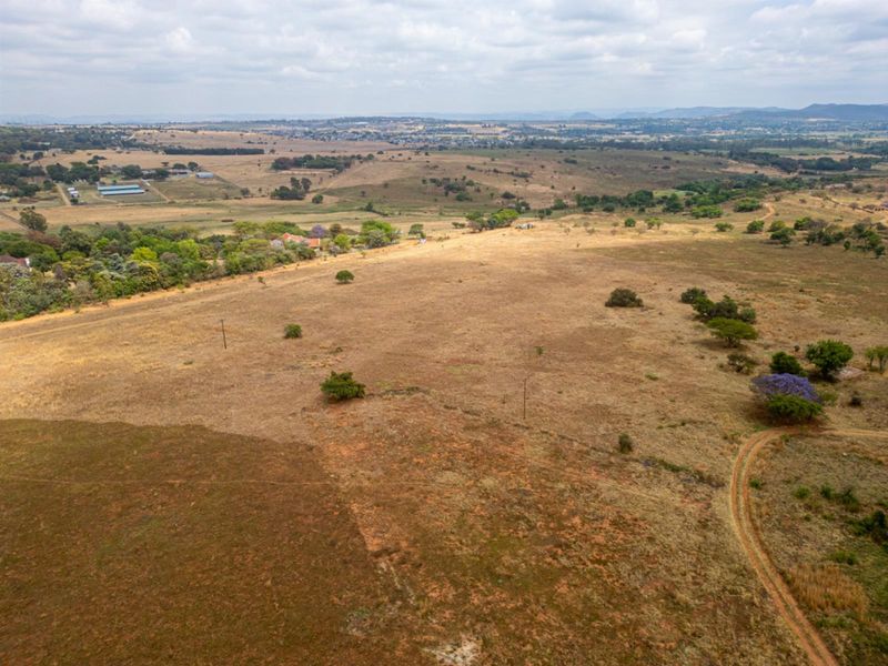 An aerial view of a large, vacant residential plot featuring natural vegetation, a dirt access track, and distant landscape views.