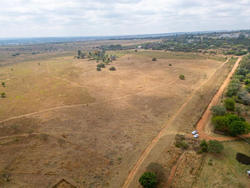 An aerial view of a large, undeveloped residential land parcel featuring open grassland and a dirt access road.