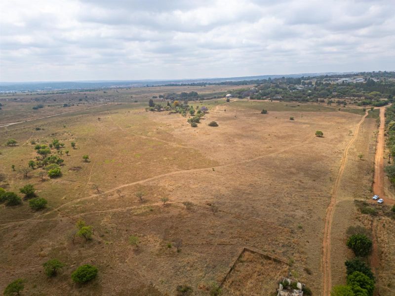 An aerial view of a large, vacant residential plot featuring natural vegetation and an unpaved access road.