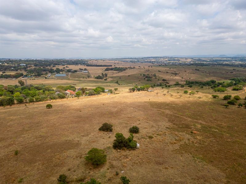 An aerial view of a large, undeveloped residential plot featuring open grassland and scattered natural vegetation in a rural setting.