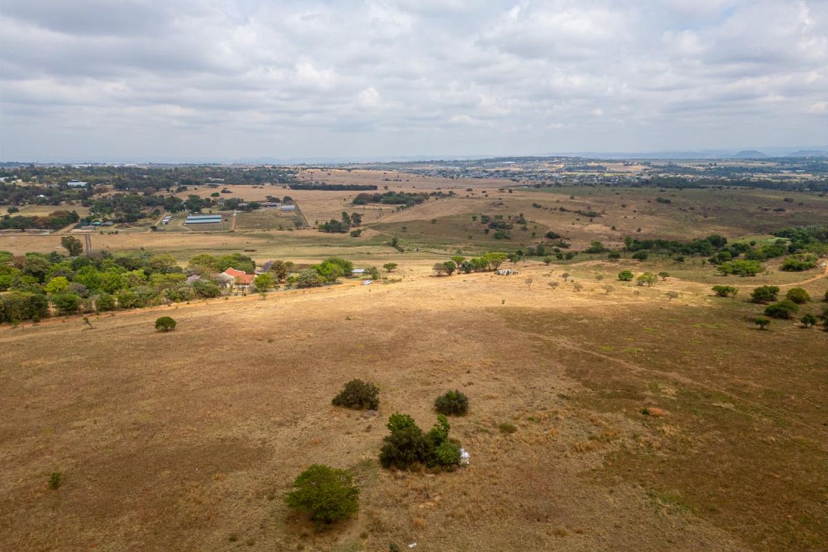 An aerial view of a large, undeveloped residential plot featuring open grassland and scattered natural vegetation in a rural setting.
