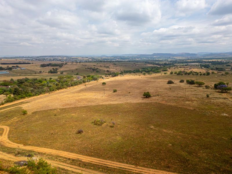 An aerial view of a large, undeveloped residential land parcel featuring open grassland, scattered trees, and a dirt access track.