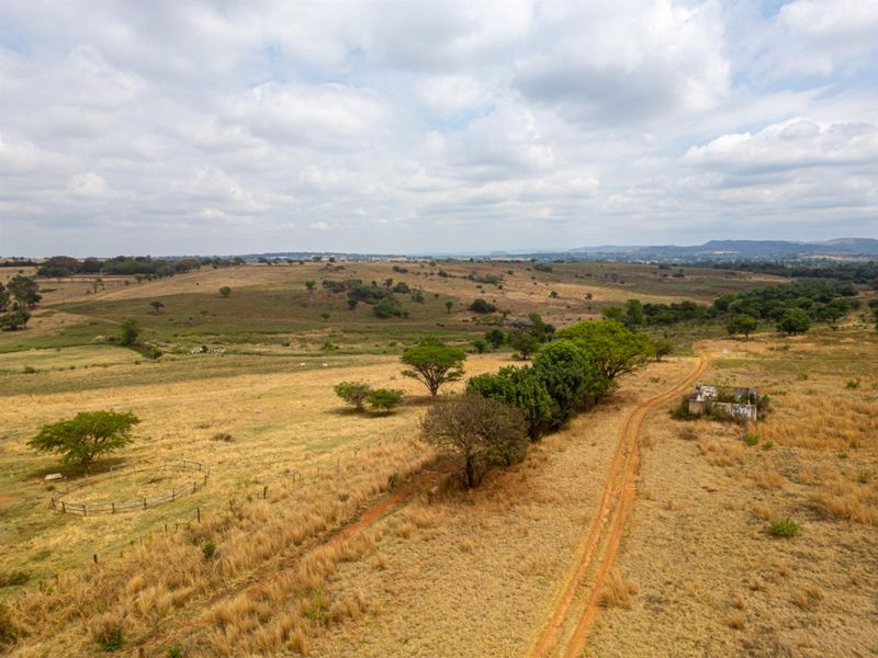 Aerial view of expansive vacant residential land featuring a dirt access track, perimeter fencing, and a small dilapidated structure on the property.
