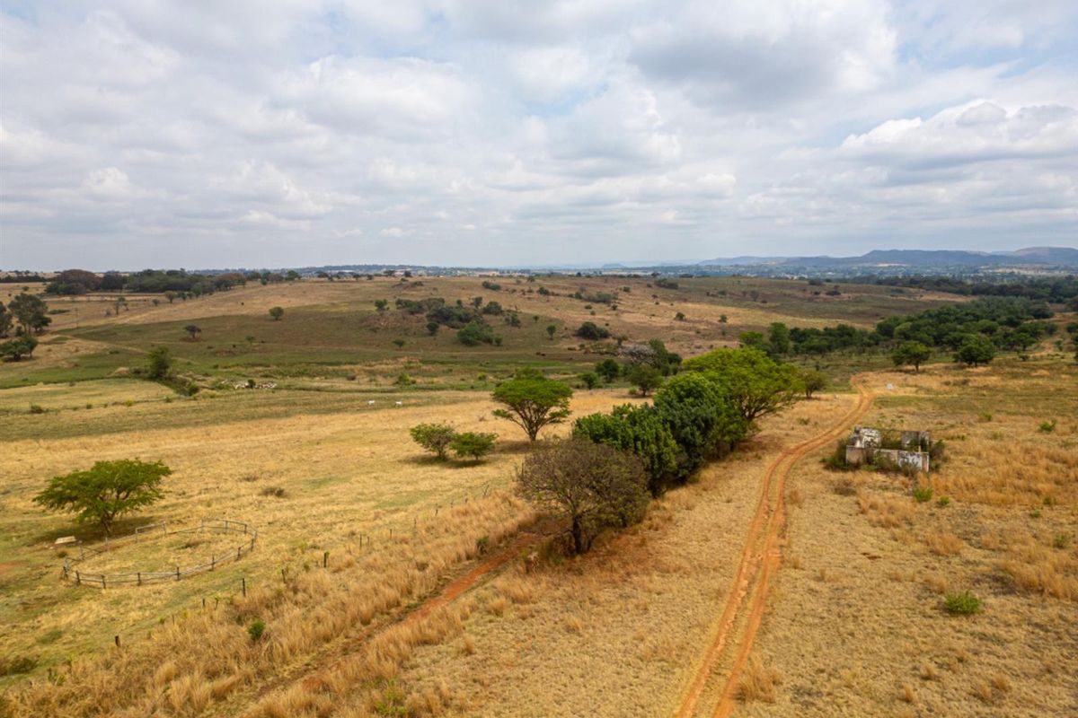 Aerial view of expansive vacant residential land featuring a dirt access track, perimeter fencing, and a small dilapidated structure on the property.