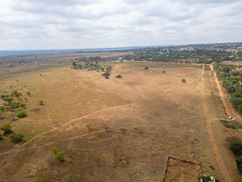 An aerial view of a large, undeveloped residential land parcel featuring natural vegetation and an unpaved access road.