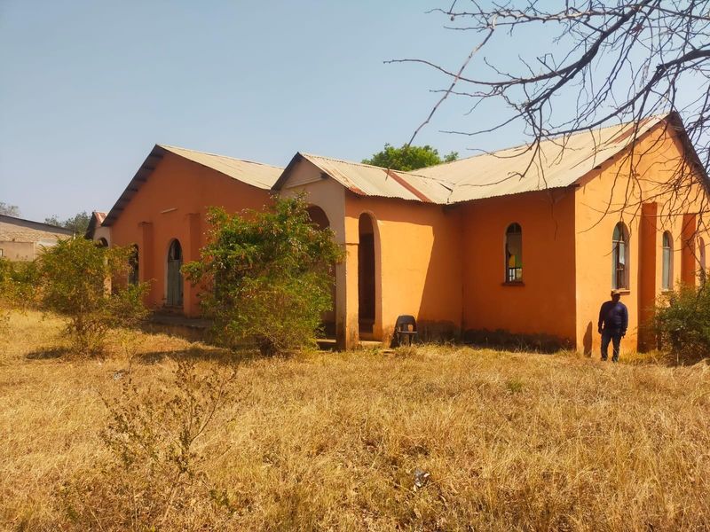 A detached commercial building featuring a corrugated metal roof and arched windows, set on a large plot with significant exterior maintenance required.