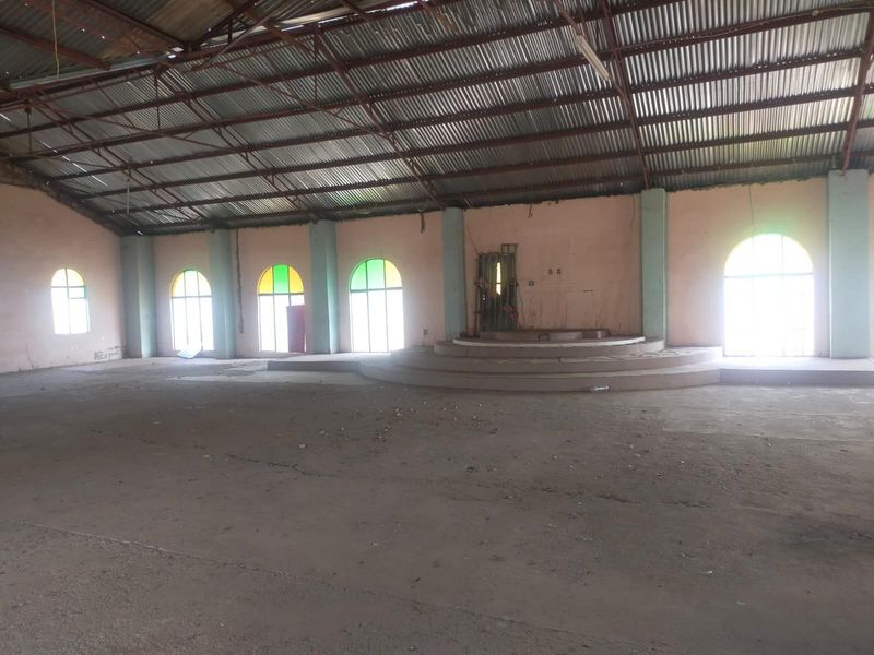 Large open-plan commercial space featuring a high corrugated metal roof, arched windows, and a central raised concrete platform.