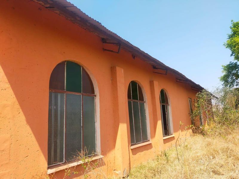 Exterior view of a commercial building featuring arched windows, masonry walls, and a corrugated metal roof, showing signs of significant wear and weathering.
