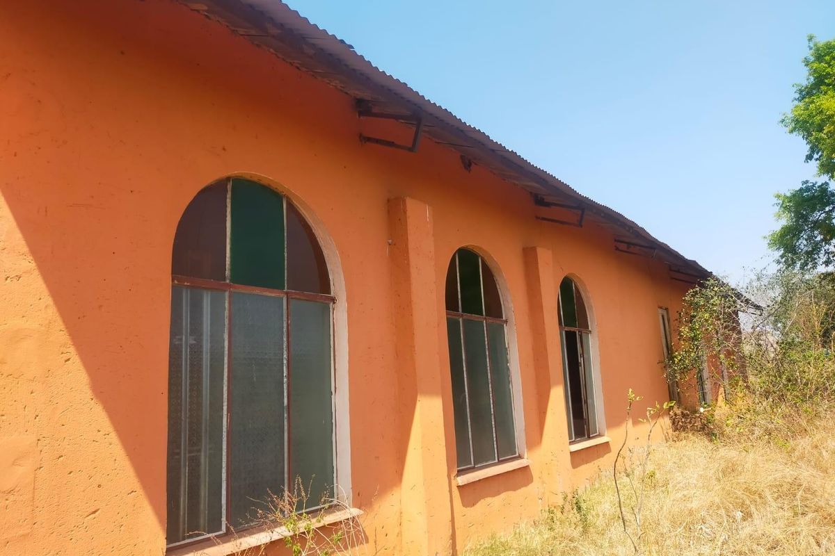 Exterior view of a commercial building featuring arched windows, masonry walls, and a corrugated metal roof, showing signs of significant wear and weathering.
