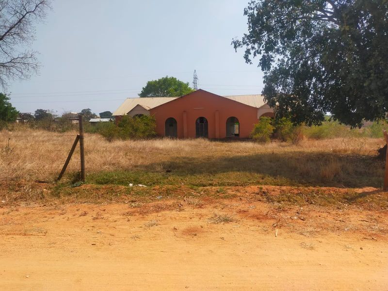 A view of a commercial building facade featuring arched entryways and a metal roof, set on a large, undeveloped plot of land.