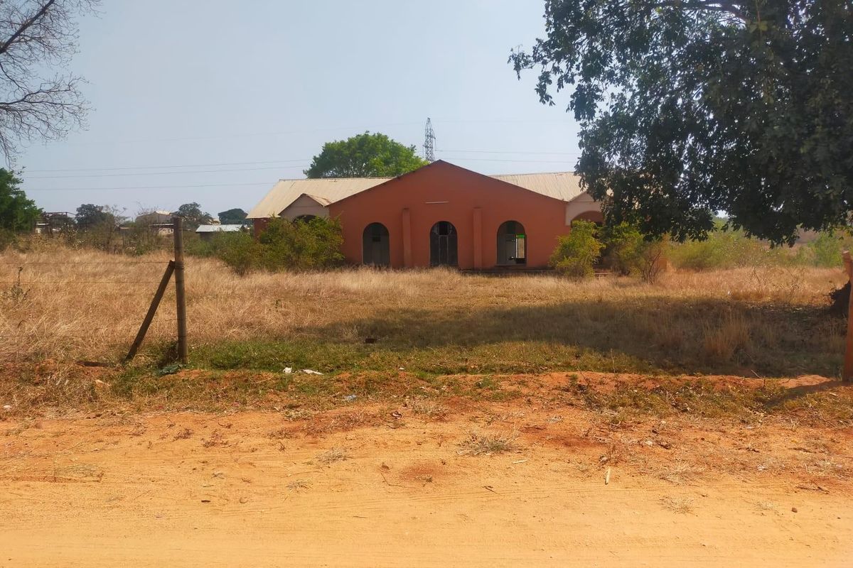 A view of a commercial building facade featuring arched entryways and a metal roof, set on a large, undeveloped plot of land.