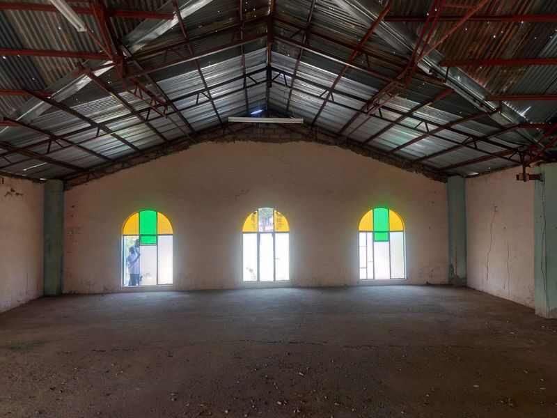A large, open-plan commercial space featuring exposed steel roof trusses, concrete flooring, and arched windows with stained glass accents.