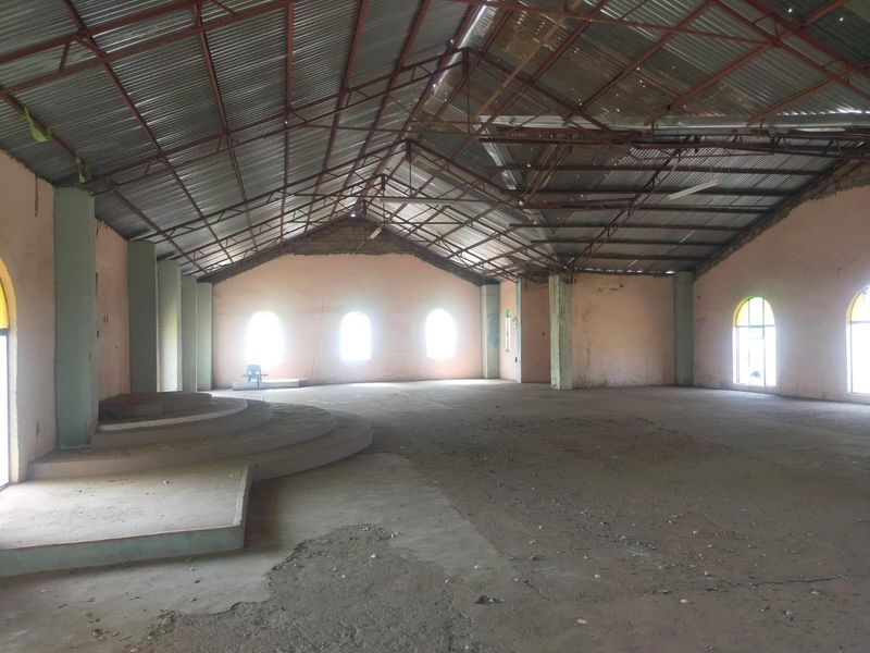 Large open-plan commercial space featuring exposed steel roof trusses, arched windows, and a raised concrete platform, suitable for various commercial or assembly uses.