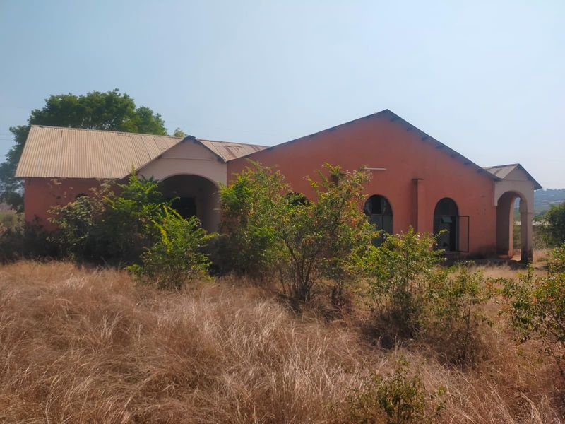 Exterior view of a commercial building featuring arched entryways and a corrugated metal roof, currently showing significant signs of neglect and weathering.