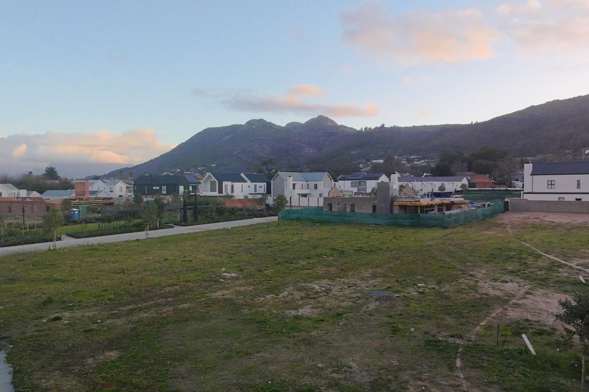 An aerial view of a residential estate under development, featuring surrounding mountain vistas and open land plots.