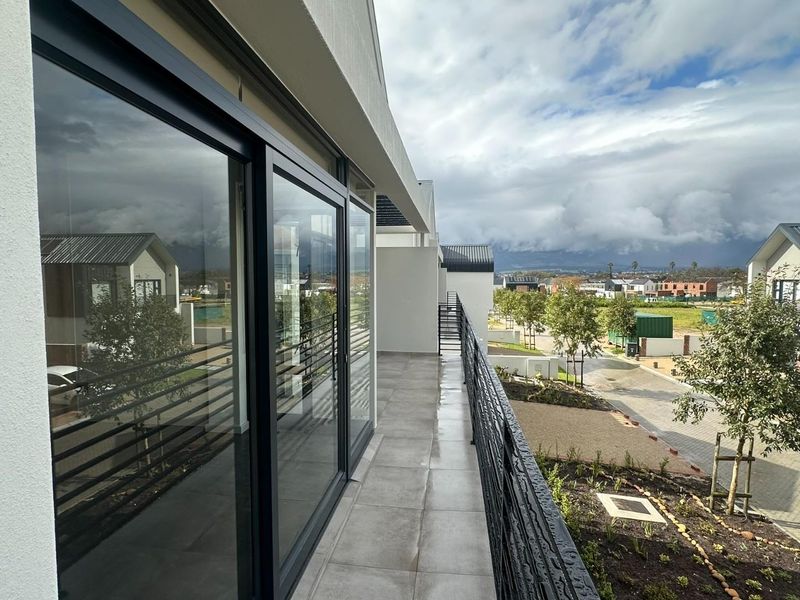 A modern, tiled balcony featuring a sleek metal balustrade and large sliding glass doors, offering an elevated view of the surrounding residential estate.