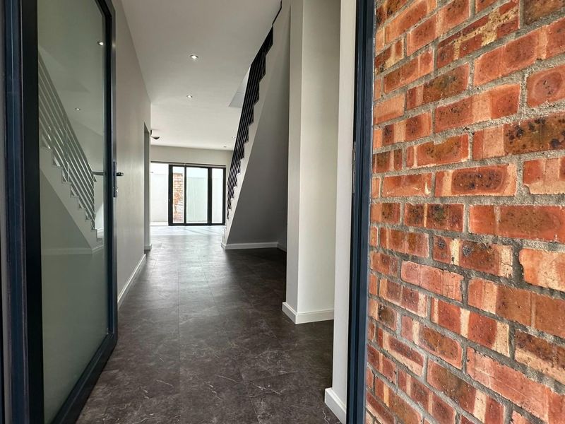 A modern, bright hallway featuring tiled flooring, a striking exposed brick wall, and a staircase leading to the upper level.