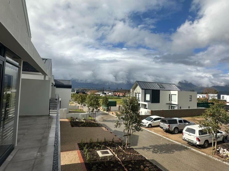 Elevated view overlooking a modern residential estate with paved driveways, landscaped garden beds, and mountain views in the background.