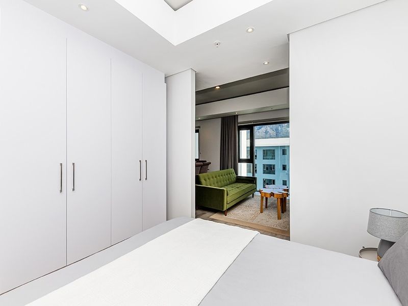 Modern bedroom featuring extensive built-in cupboards, recessed ceiling lighting, and a seamless transition to an adjacent living area with mountain views.