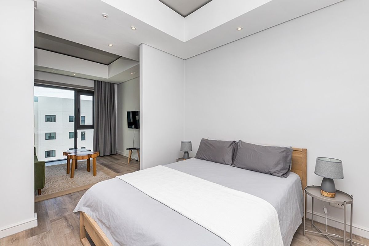 Modern bedroom featuring recessed ceiling lighting, laminate flooring, and a sliding glass door leading to an adjacent living area.