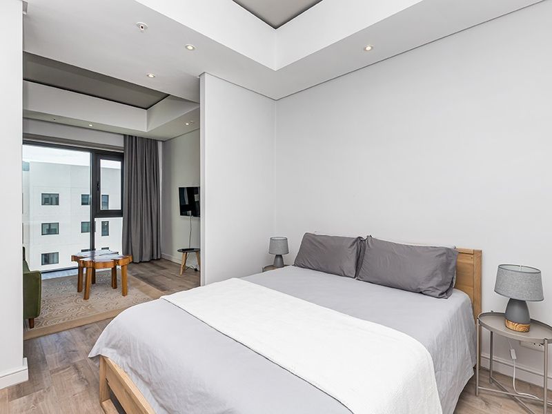 Modern bedroom featuring recessed ceiling lighting, laminate flooring, and a sliding glass door leading to an adjacent living area.