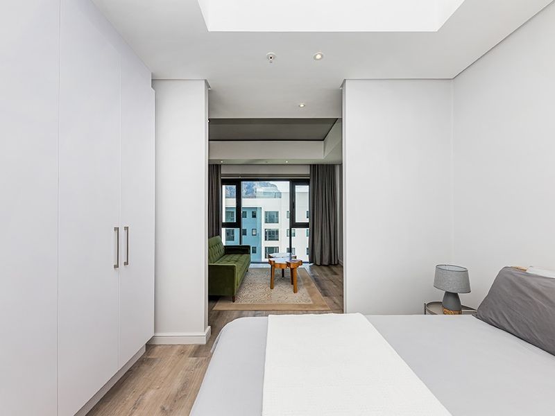 Modern bedroom featuring sleek built-in cupboards, recessed lighting, and laminate flooring, with an open transition to an adjacent living area.
