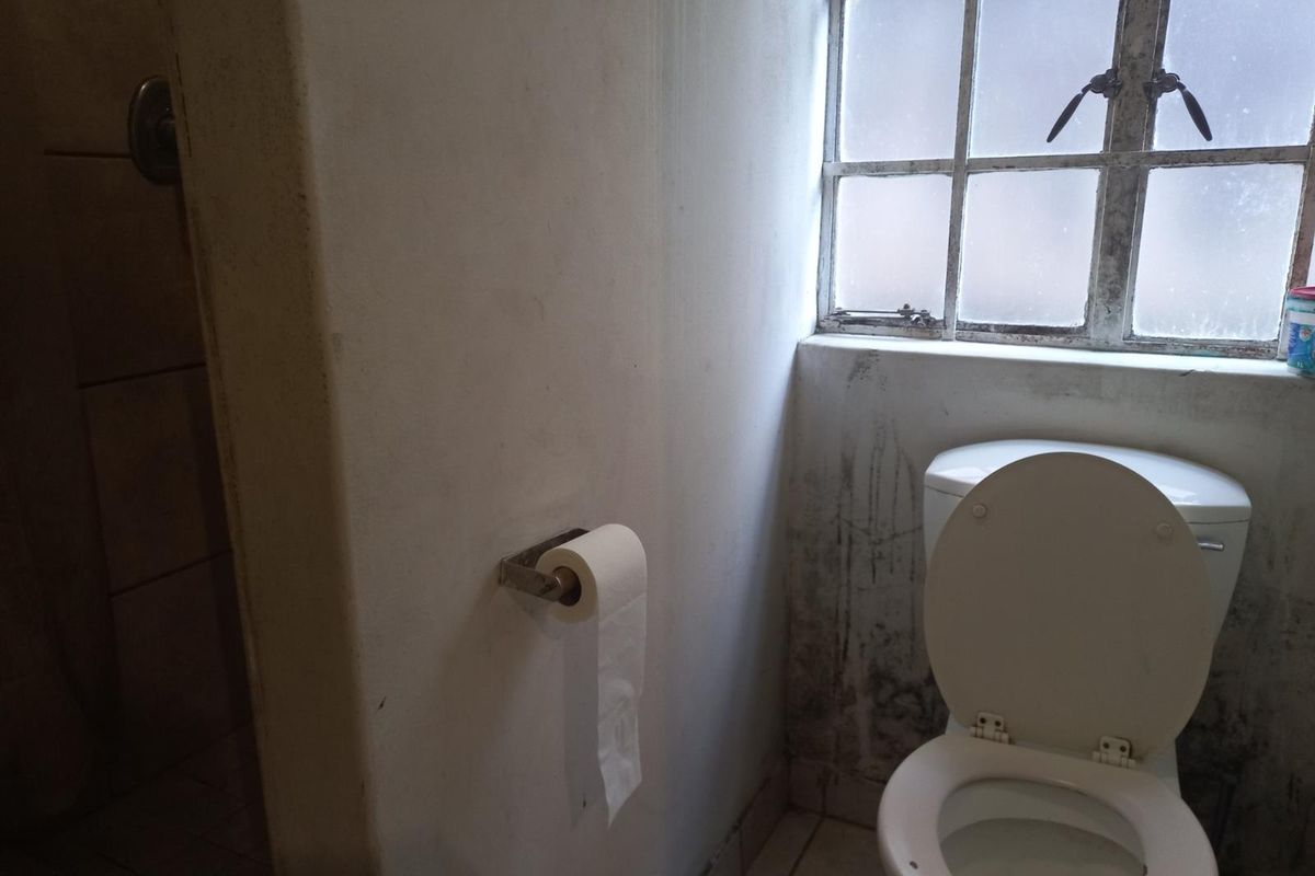 A bathroom featuring a toilet and a window with visible wall staining and signs of wear on the finishes.