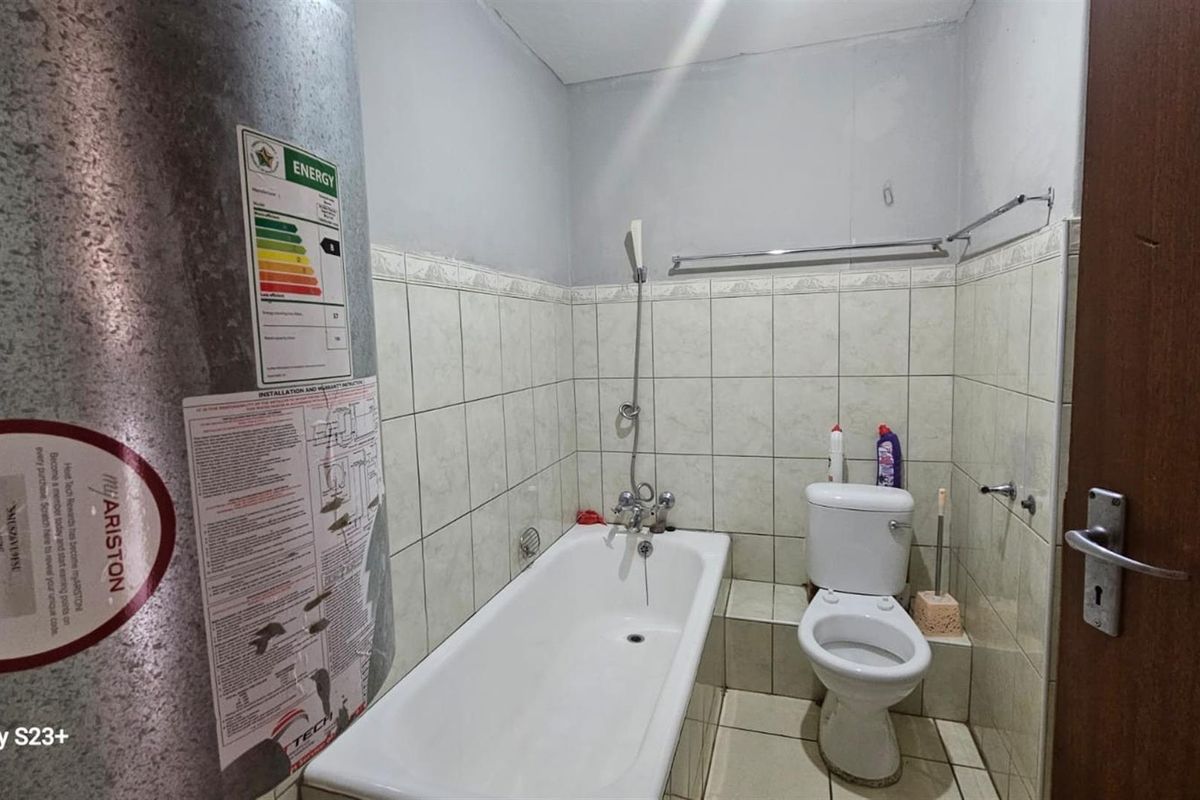 A functional bathroom featuring a standard bathtub, toilet, and an exposed electric water heater unit.
