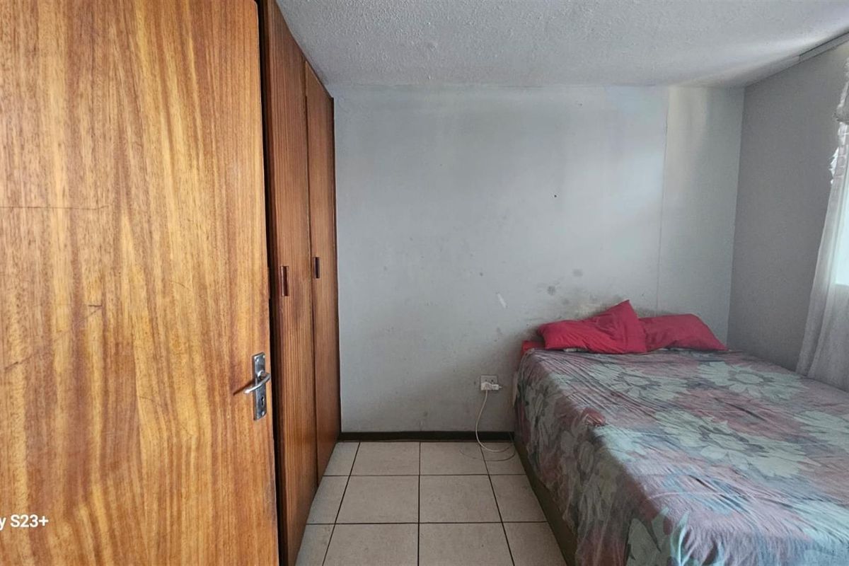 A bedroom featuring built-in wooden cupboards and tiled flooring, requiring cosmetic updates to the wall finishes.