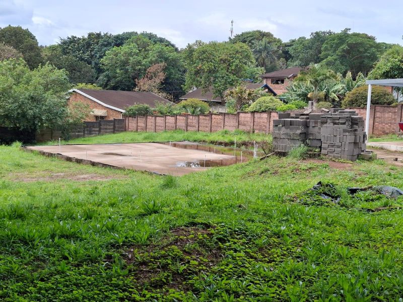Vacant residential land featuring a concrete foundation slab, brick boundary walls, and established surrounding greenery.