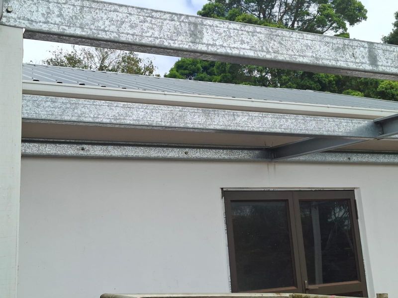Exterior view of a residential property showing exposed galvanized steel structural framing and metal roofing over a windowed wall section.