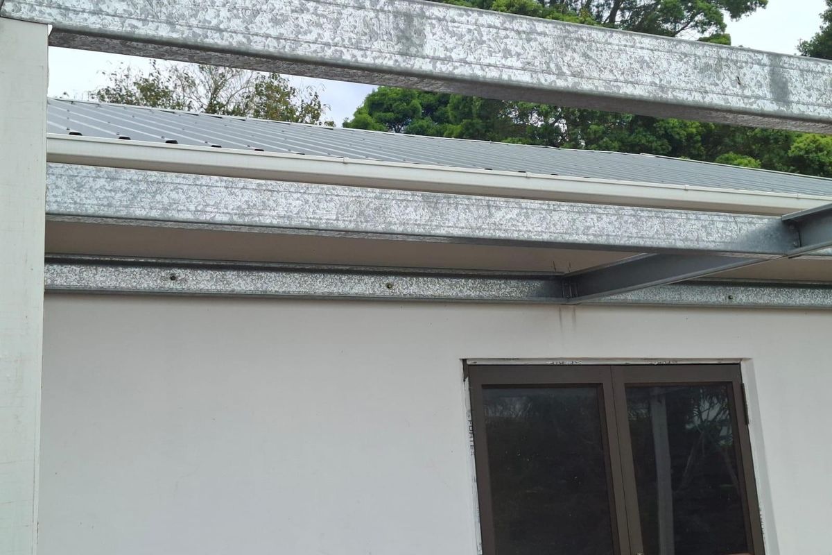 Exterior view of a residential property showing exposed galvanized steel structural framing and metal roofing over a windowed wall section.