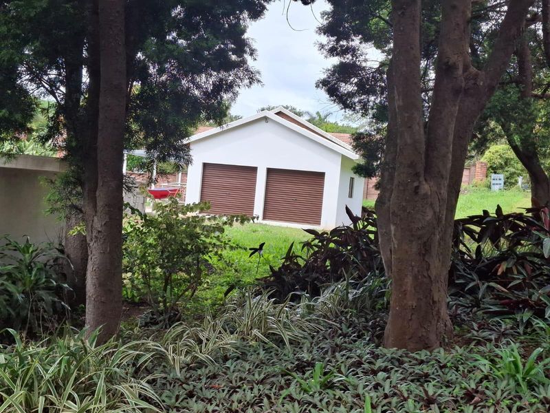 A view of a detached double garage with roller shutter doors, situated within a well-maintained garden setting.