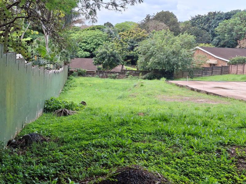 A vacant residential plot featuring a perimeter wall, concrete slab, and established greenery, offering a blank canvas for future development.