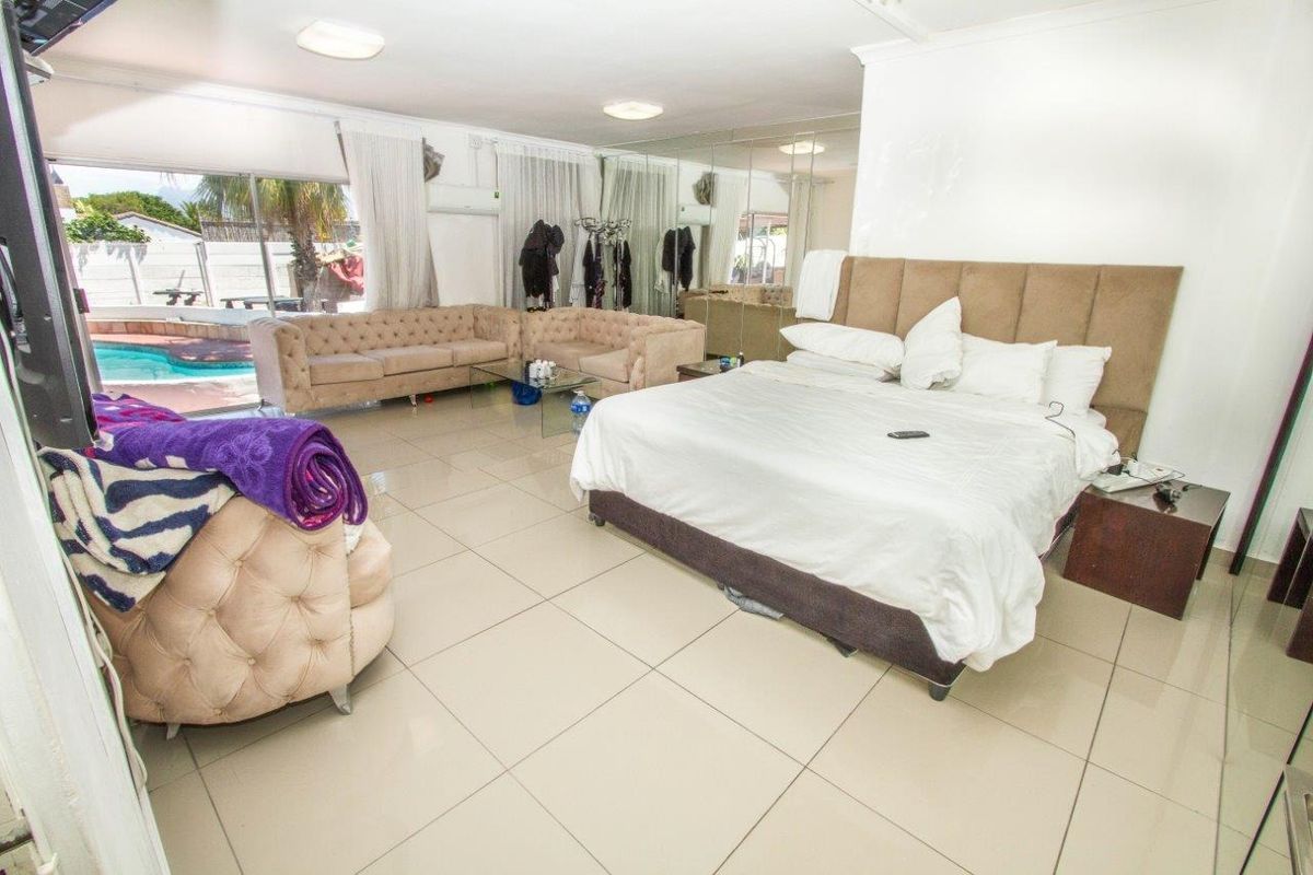 Spacious bedroom featuring large format floor tiles, mirrored wall panels, and direct access to the outdoor pool area through sliding glass doors.