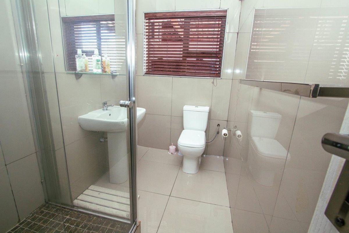 A functional bathroom featuring a glass-enclosed shower, pedestal basin, and toilet with neutral wall and floor tiling.