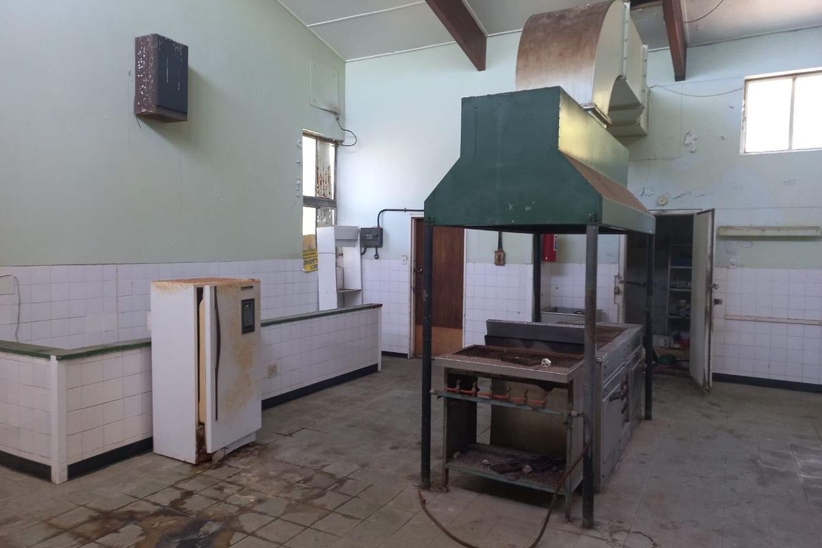 Commercial kitchen space featuring a large industrial extractor hood, tiled splashbacks, and tiled flooring, requiring significant refurbishment and modernization.