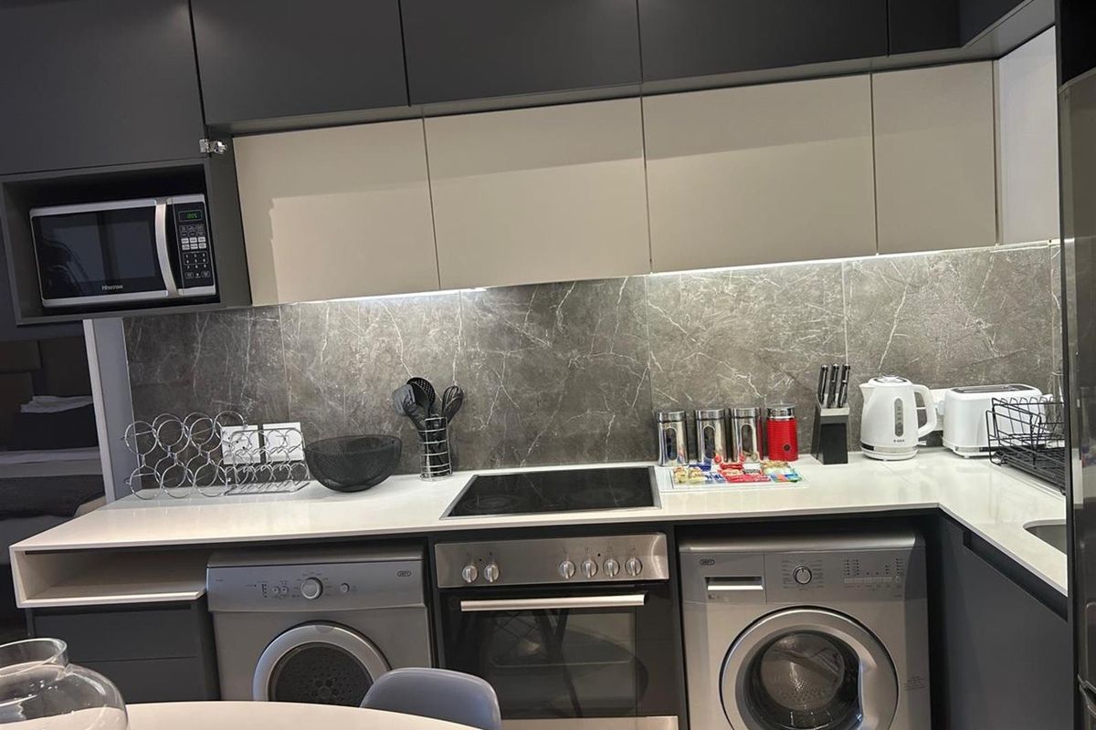Modern kitchen featuring sleek dark cabinetry, stone-look splashback, integrated oven, electric cooktop, and built-in microwave with under-cabinet lighting.