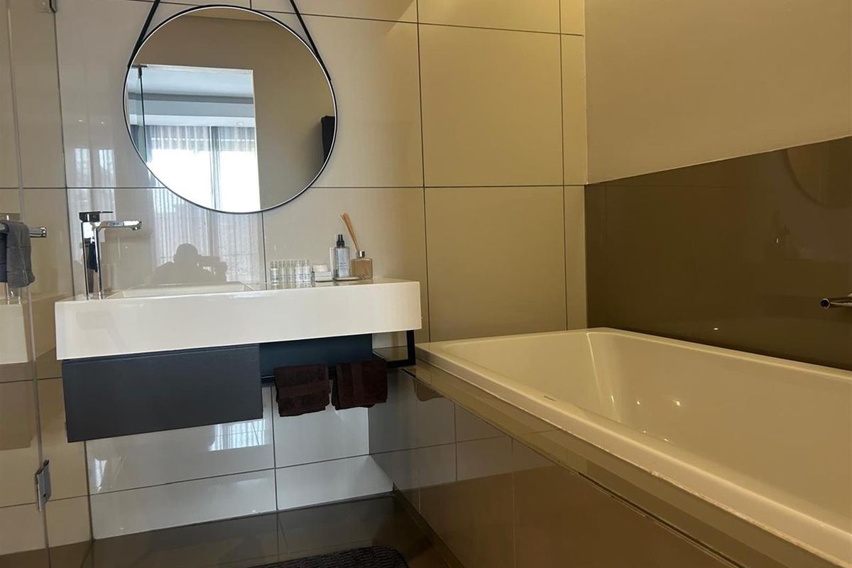 Modern bathroom featuring a wall-mounted vanity with integrated basin, sleek chrome faucet, and a built-in bathtub with neutral wall tiling.