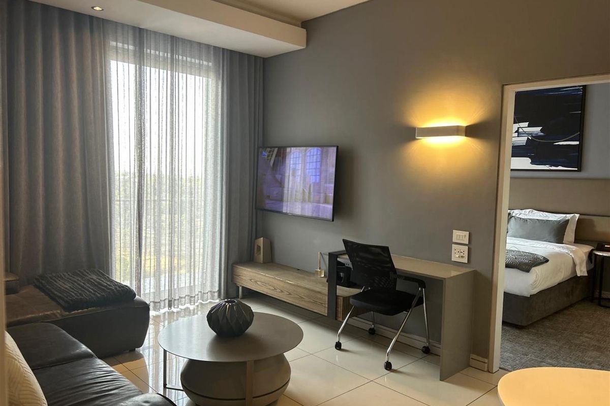 Modern living area featuring tiled flooring, recessed ceiling lighting, wall-mounted lighting, and a sliding door leading to a balcony, with an adjacent bedroom.