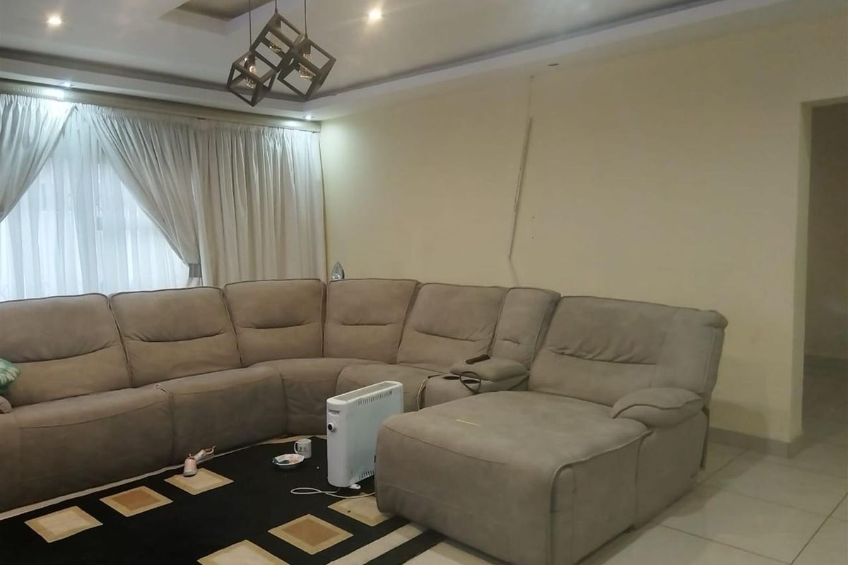 A spacious living room featuring tiled flooring, recessed ceiling lighting, and a large window with curtains.