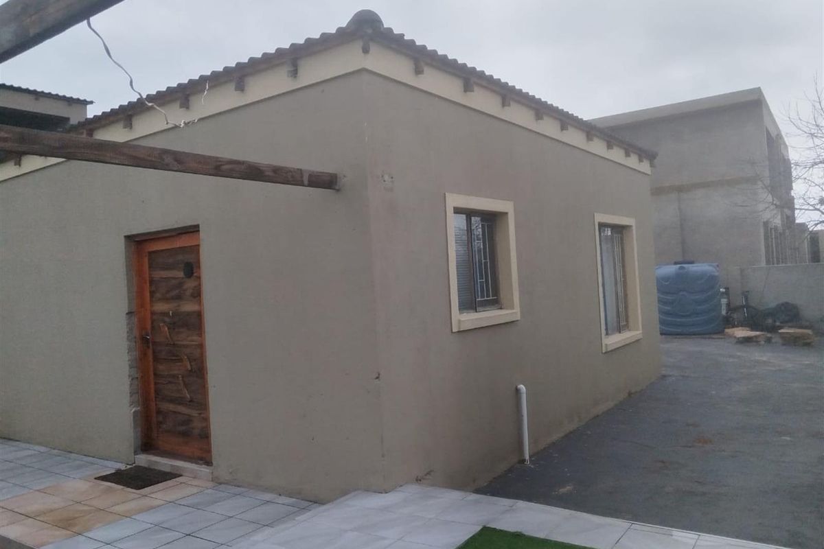 Exterior view of a single-story dwelling featuring a tiled roof, plastered walls, wooden entrance door, and paved outdoor area.