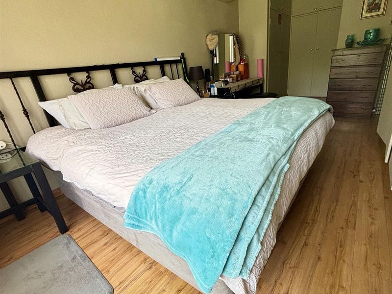 A bedroom featuring laminate flooring, built-in cupboards for storage, and a wall-mounted air conditioning unit for climate control.