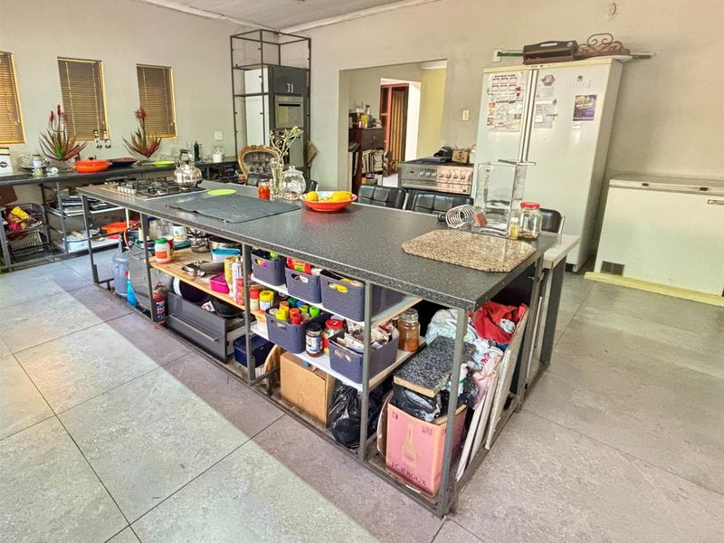 Spacious kitchen featuring a large central island with a gas hob, tiled flooring, and built-in oven, offering significant potential for modernization and layout optimization.