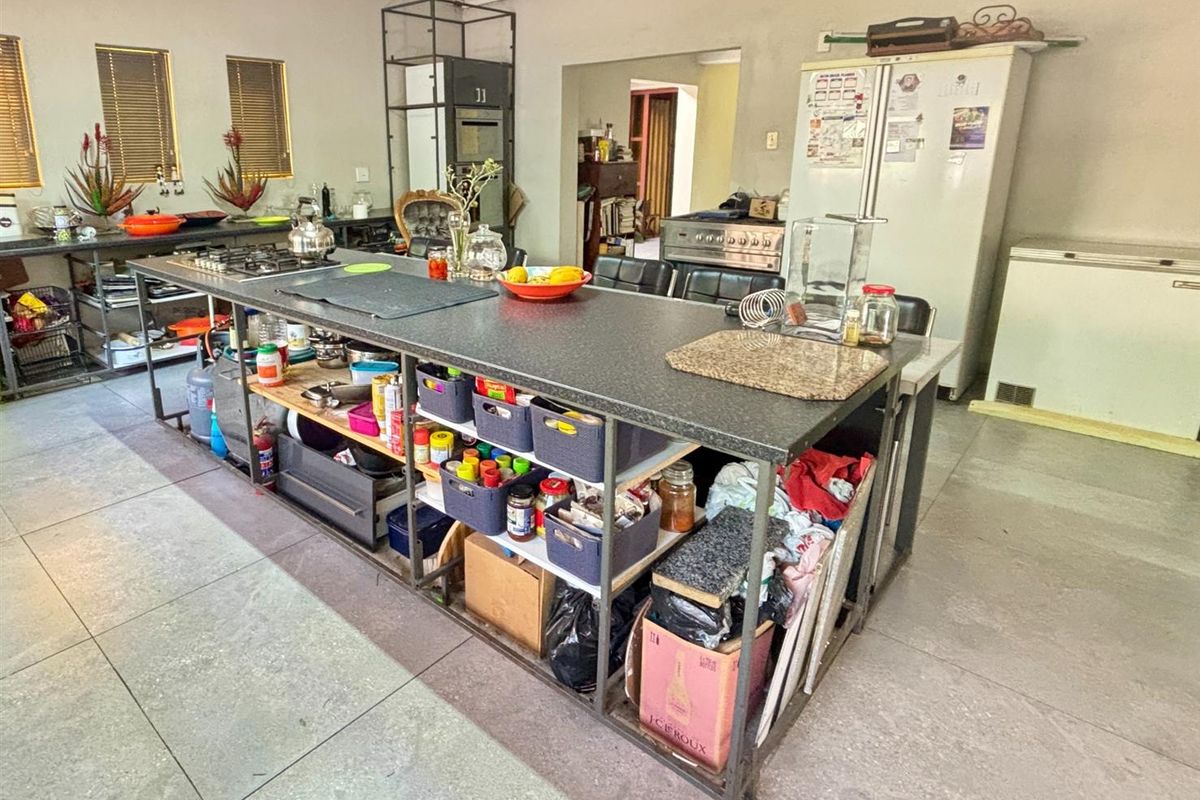 Spacious kitchen featuring a large central island with a gas hob, tiled flooring, and built-in oven, offering significant potential for modernization and layout optimization.