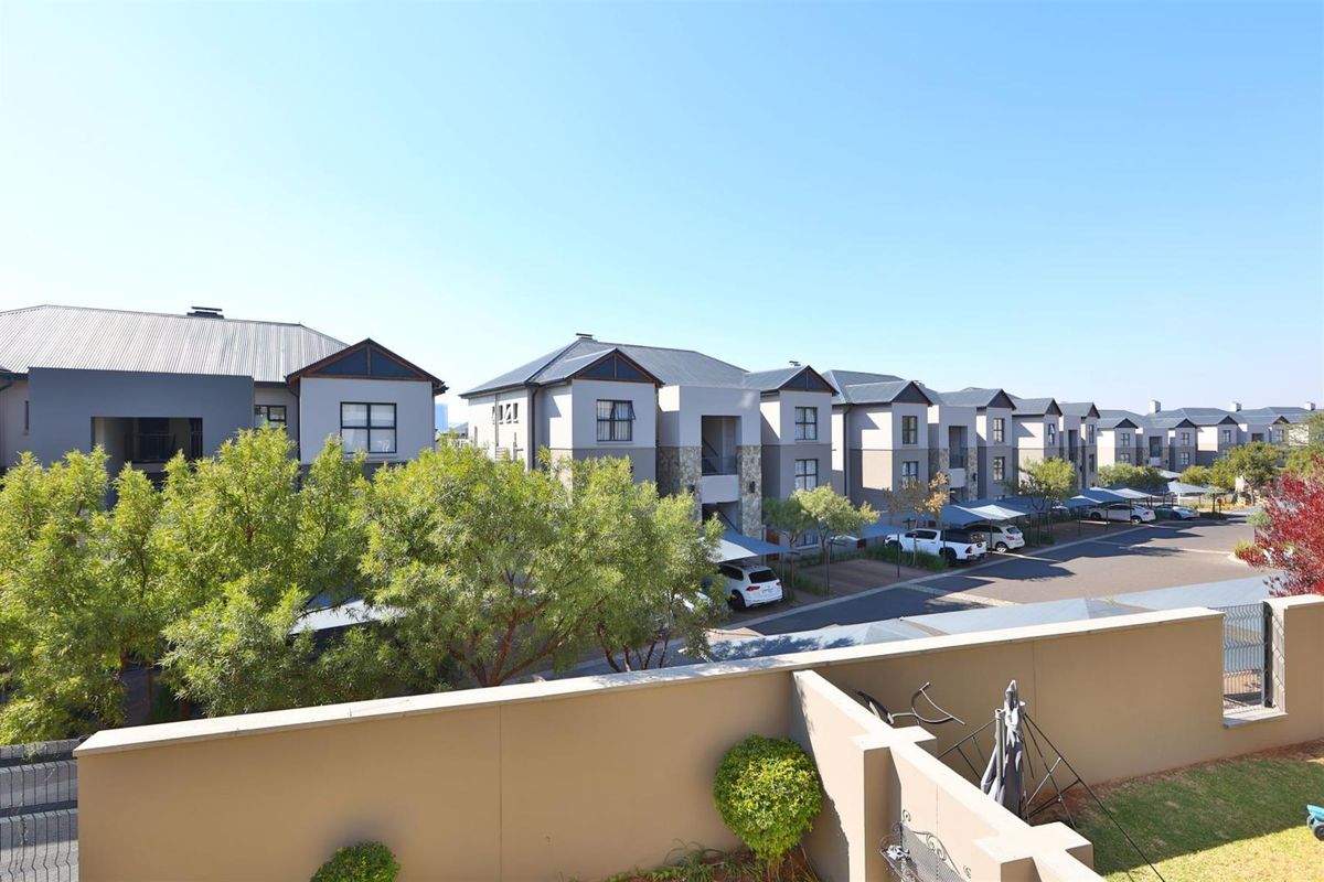 An elevated view of the apartment complex showing the rear building facades, paved parking areas with carports, and surrounding landscaped grounds.