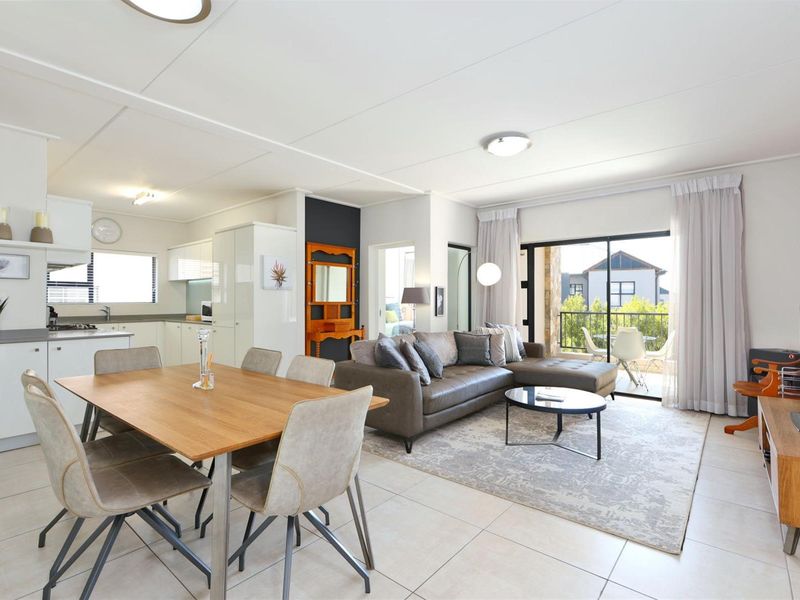 Spacious open-plan living and dining area featuring tiled floors, a modern kitchen with built-in cabinetry, and direct access to a private balcony.