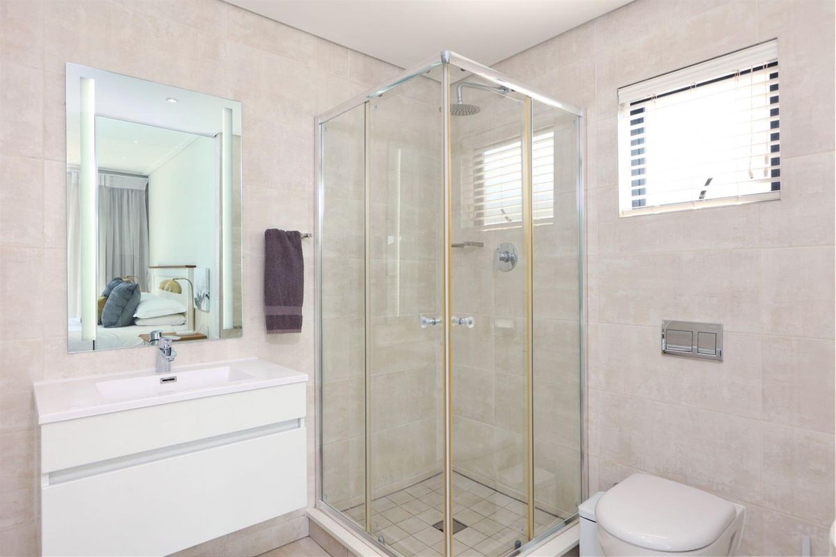 Modern bathroom featuring a vanity with basin, a glass-enclosed shower, and a wall-hung toilet with neutral tiled finishes throughout.