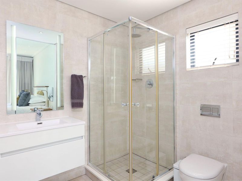Modern bathroom featuring a vanity with basin, a glass-enclosed shower, and a wall-hung toilet with neutral tiled finishes throughout.