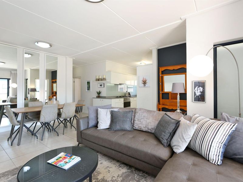 Spacious open-plan living and dining area featuring tiled floors, modern kitchen cabinetry with built-in appliances, and decorative mirrored wall panels.